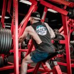 man in gray t-shirt and blue denim jeans sitting on red metal bar